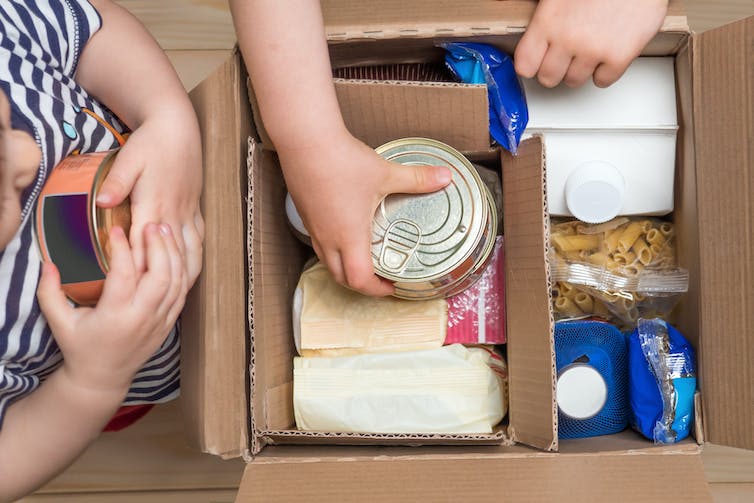 De jeunes enfants mettent des aliments secs et en conserve dans une boîte.