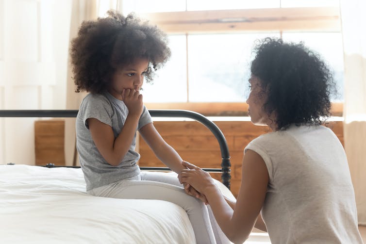 Une femme noire tient la main d’une jeune fille noire assise sur un lit