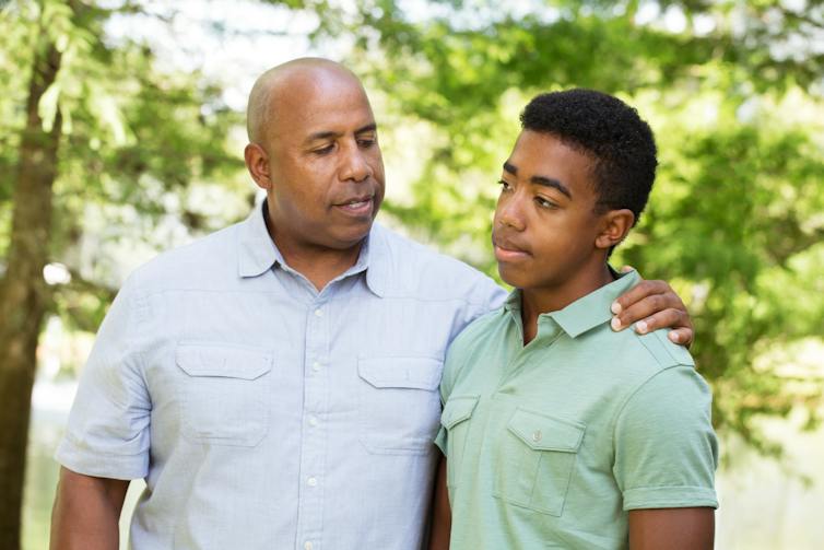 Un homme avec son bras autour d'un adolescent, à l'extérieur