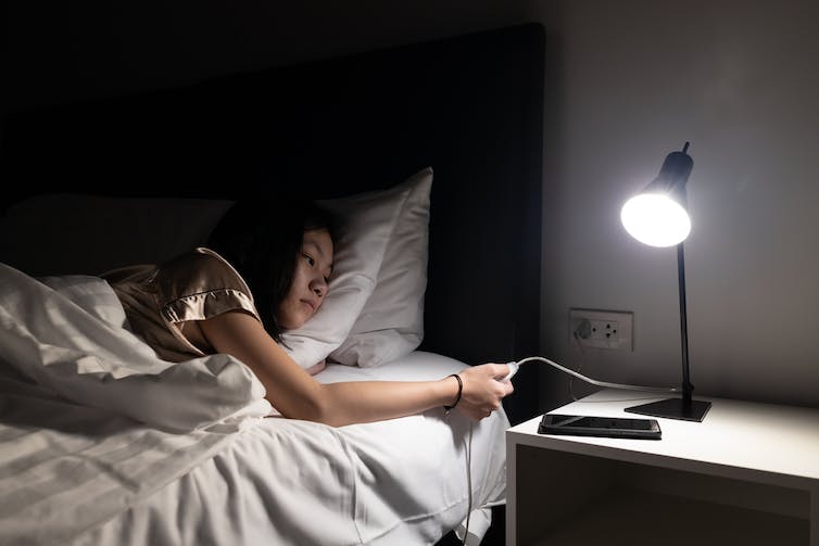 Une jeune fille touche l’interrupteur d’une lampe sur sa table de chevet.