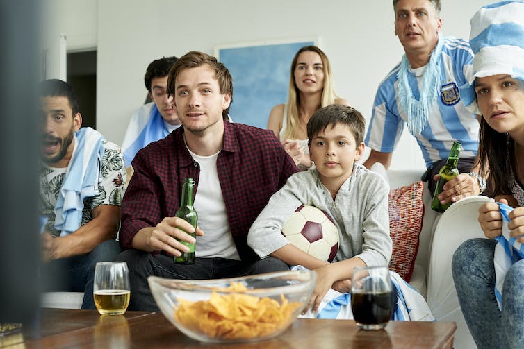 famille, certains avec des bières, regardant un match de football à la télévision, un garçon tient le ballon