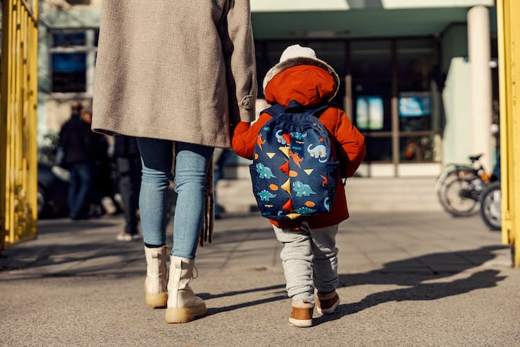 Une mère entrant à la maternelle avec son enfant d'âge préscolaire.