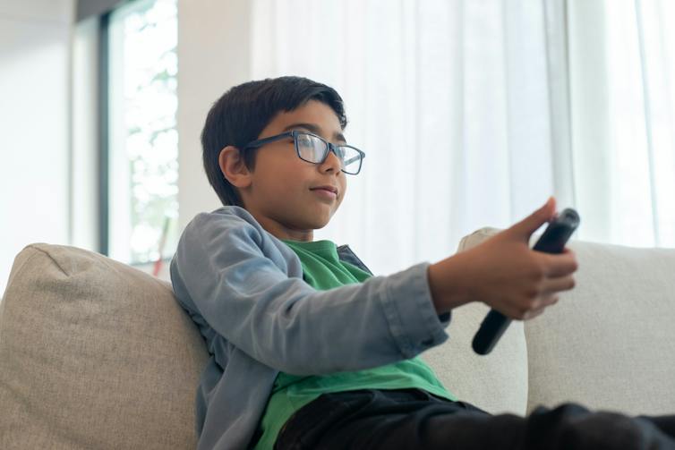 Un jeune garçon est assis sur un canapé avec une télécommande de télévision.