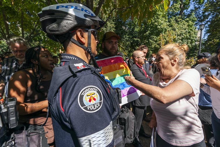 Deux femmes se disputent lors d'une manifestation.  Un policier se tient à leurs côtés.