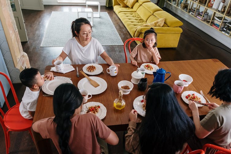 Une famille vue assise à une table en train de manger un repas.