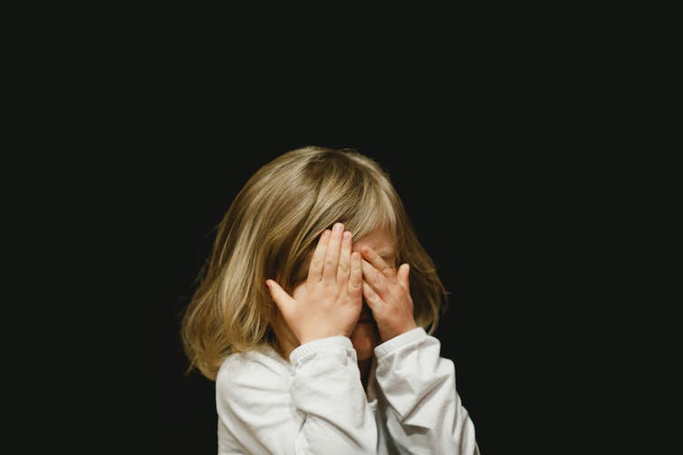 Une jeune fille se couvre le visage de ses mains.