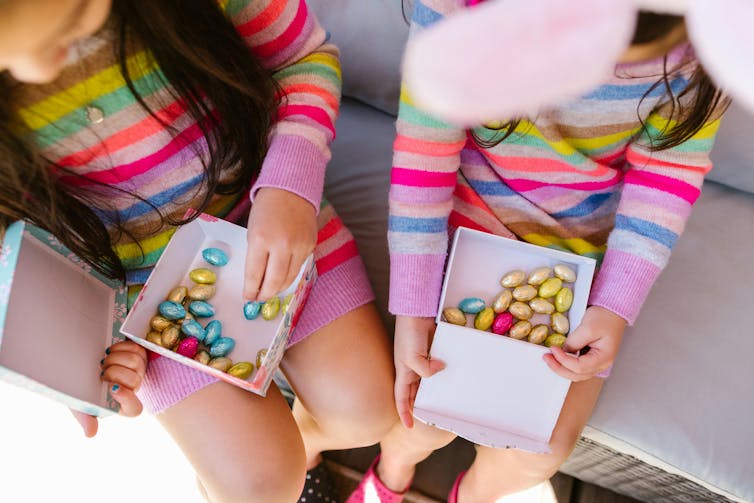 Deux jeunes enfants tiennent des boîtes contenant de petits œufs en chocolat emballés dans du papier aluminium.