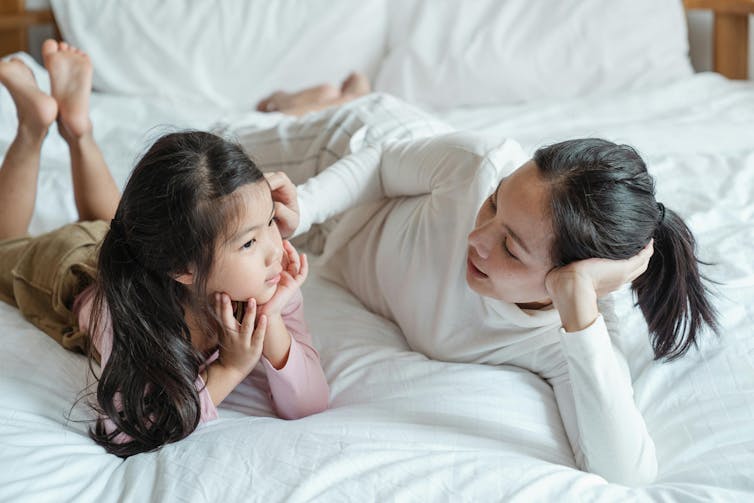 Une mère et sa fille sont allongées sur un lit et se parlent.