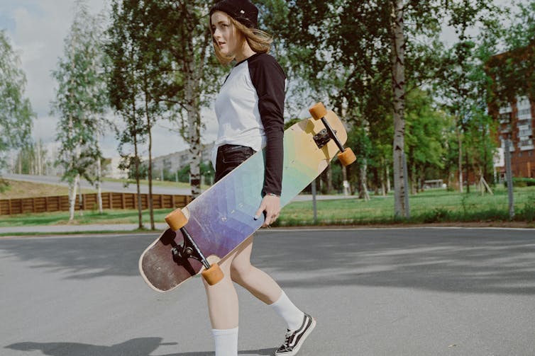 Un adolescent aux cheveux longs porte une planche à roulettes.