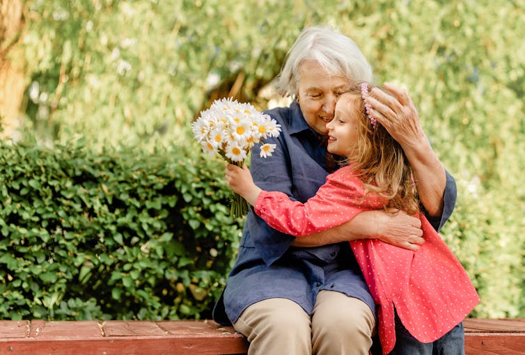Une femme âgée embrasse une jeune fille portant un bouquet de fleurs