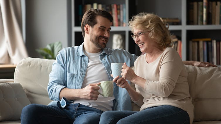 Un homme est assis avec une femme sur un canapé, tous deux portent des tasses à café