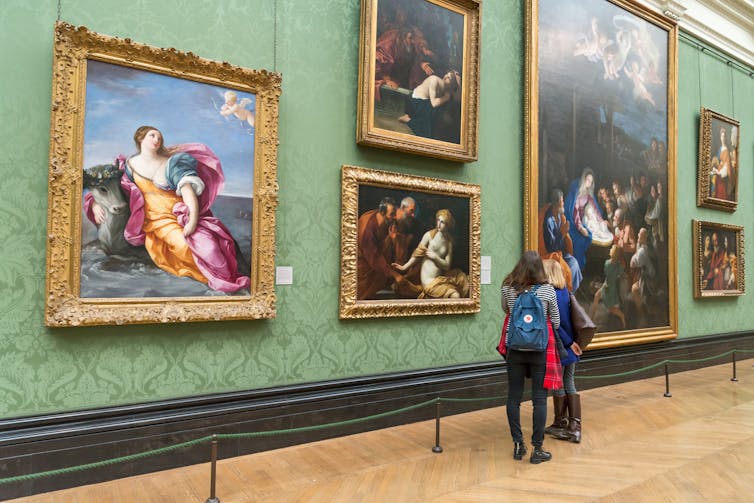 Deux personnes regardent un mur de galerie de peintures.