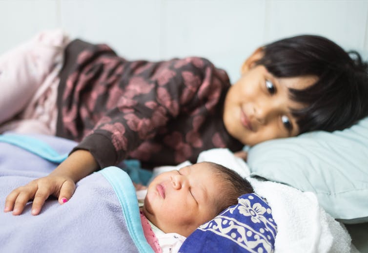 Un enfant a une main posée sur le ventre d'un nourrisson.