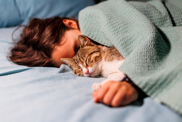 Un jeune homme dort à côté d'un chat endormi.