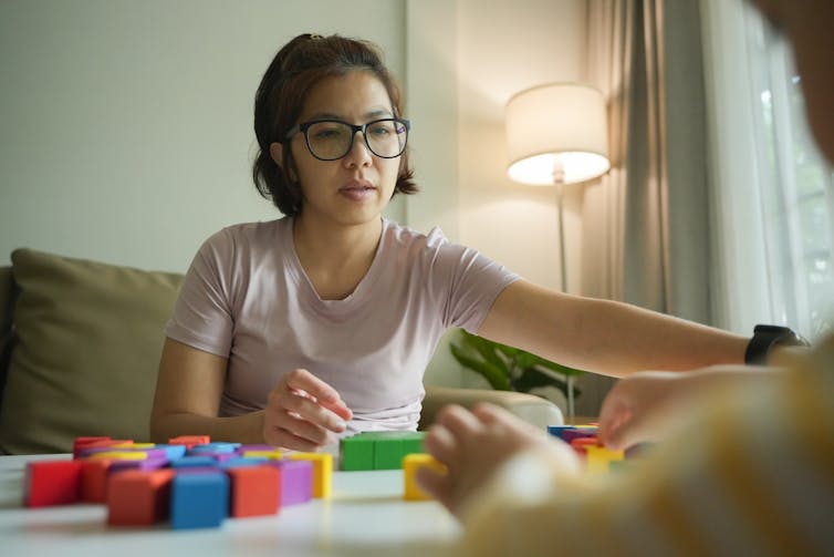 Une femme cherche un bloc sur une table. Un enfant est de l'autre côté.