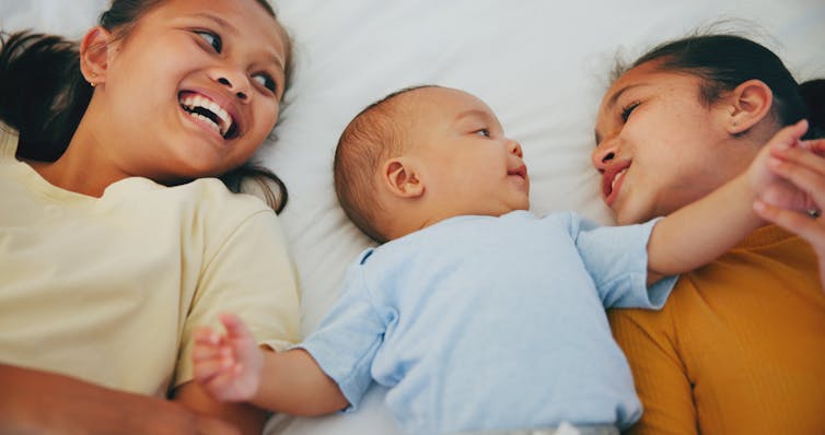 Deux enfants plus âgés couchés des deux côtés d’un bébé.