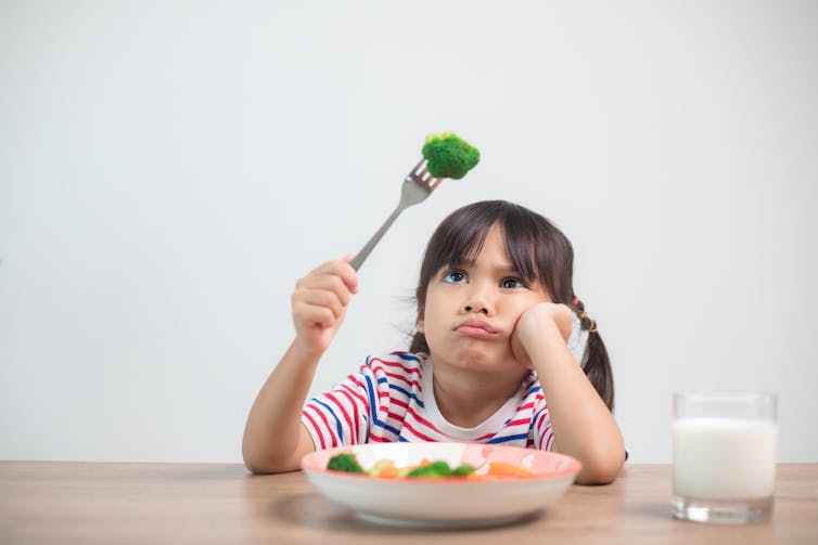 Un enfant fait une grimace mécontente en regardant un fleuron de brocoli sur sa fourchette