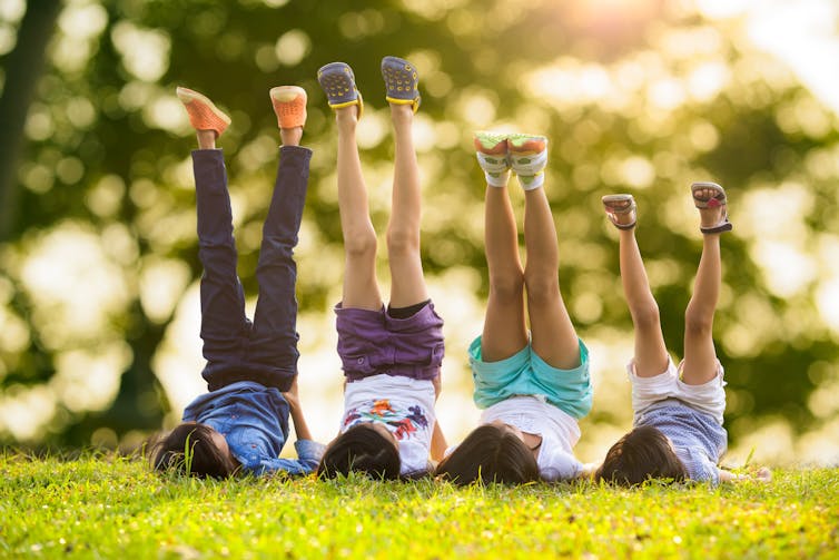 Quatre enfants se trouvent sur l'herbe avec leurs jambes en l'air.