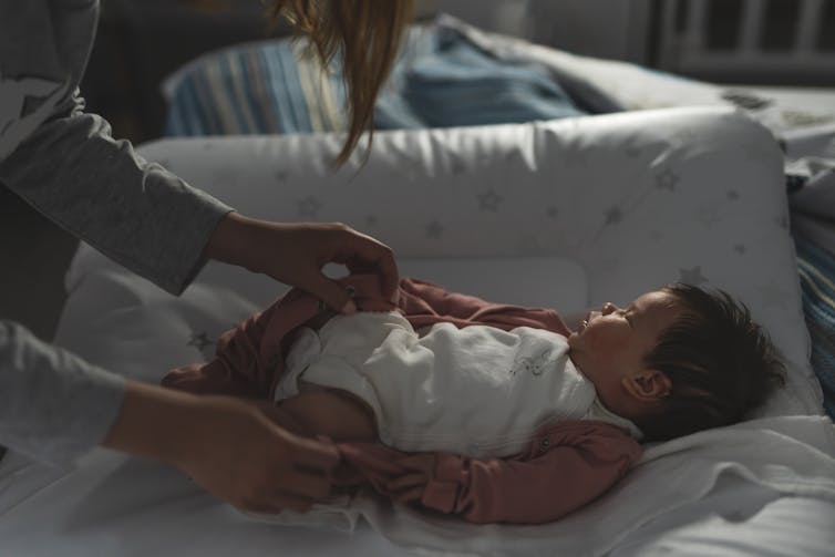 Mère qui s'occupe de bébé la nuit, bébé endormi sur un changement de tapis