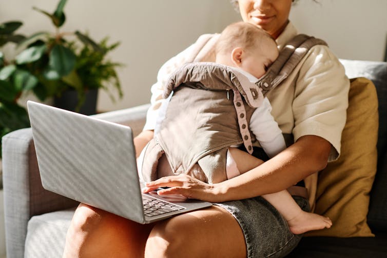Femme avec bébé dans une pochette de transporteur Types sur ordinateur portable.