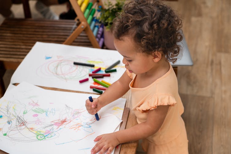Un jeune enfant dessine avec des crayons.