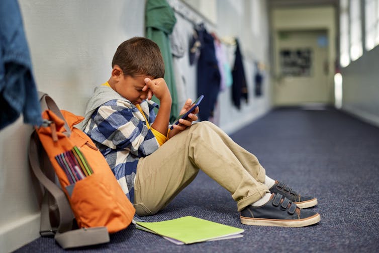 Un jeune garçon est assis sur le sol d'un couloir d'école avec sa main sur sa tête