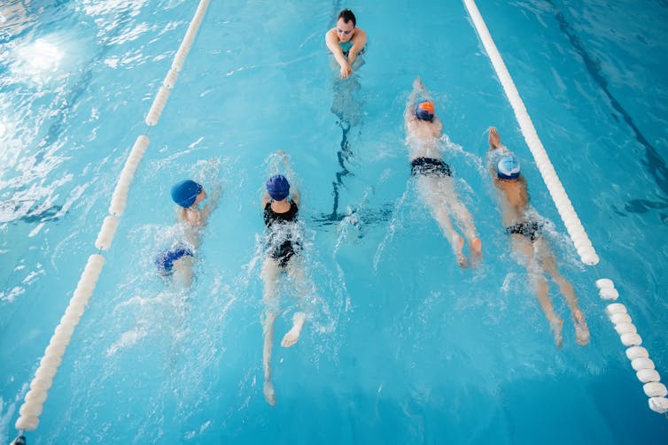 Un groupe de quatre enfants plus âgés a une leçon dans une piscine avec un enseignant.