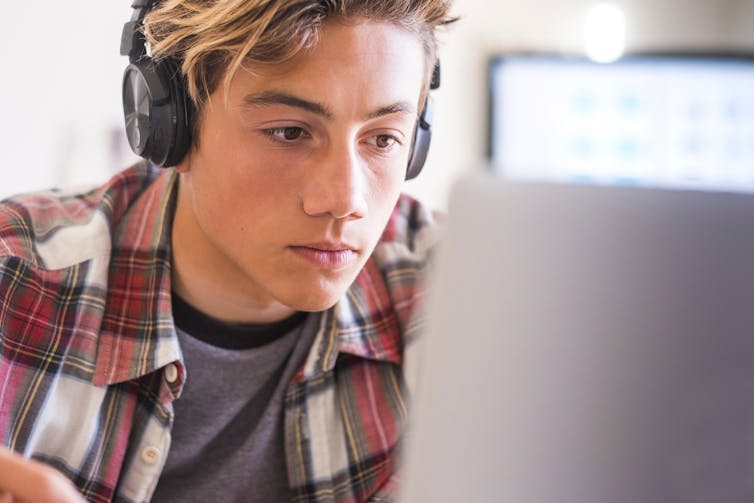 Un adolescent portant des écouteurs, regardant un écran.
