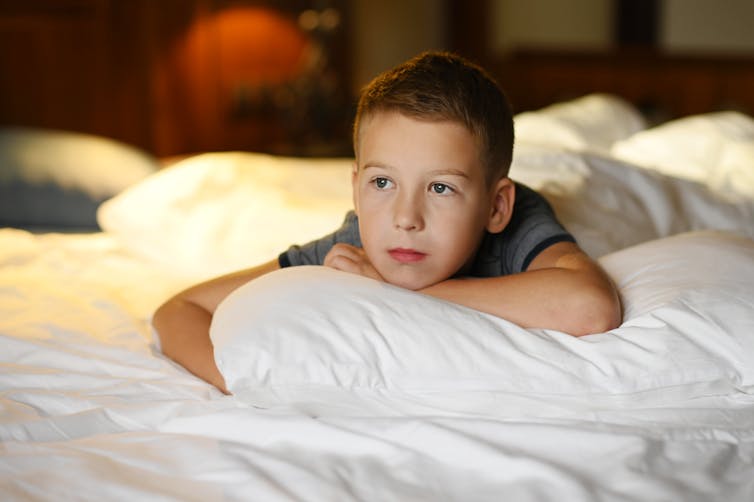 Un jeune garçon est allongé sur un oreiller sur un lit.