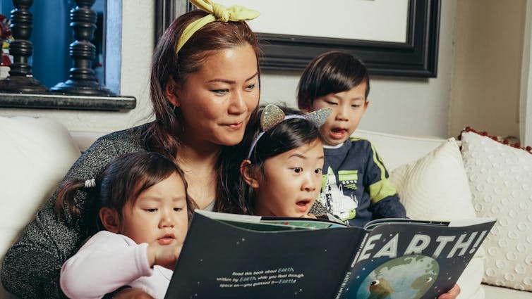 Une femme lit un livre sur la Terre à trois petits enfants.