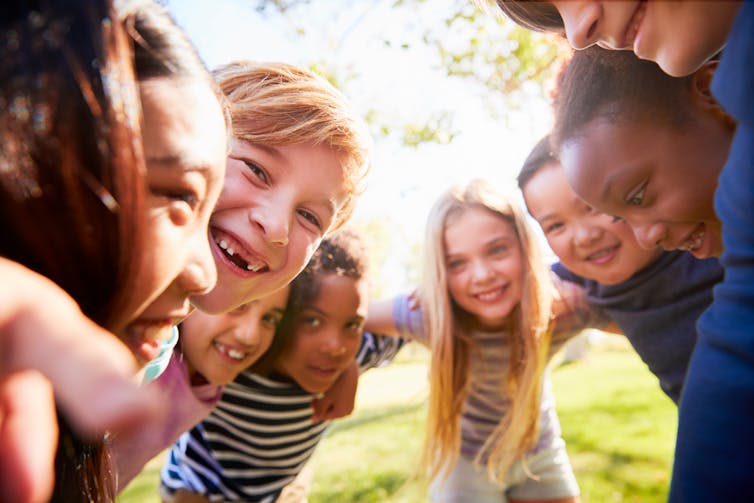 Un groupe d'enfants se met les bras les uns dans les autres, souriant.