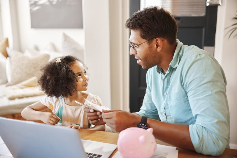Avec une tirelire au premier plan, un homme qui tient de l'argent parle à une jeune fille des finances.