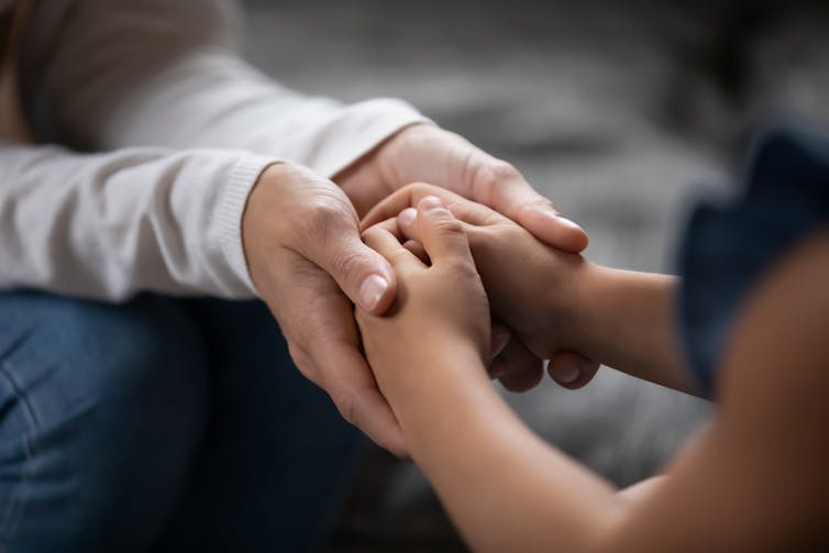 Mains adultes tenant les mains d'un enfant.