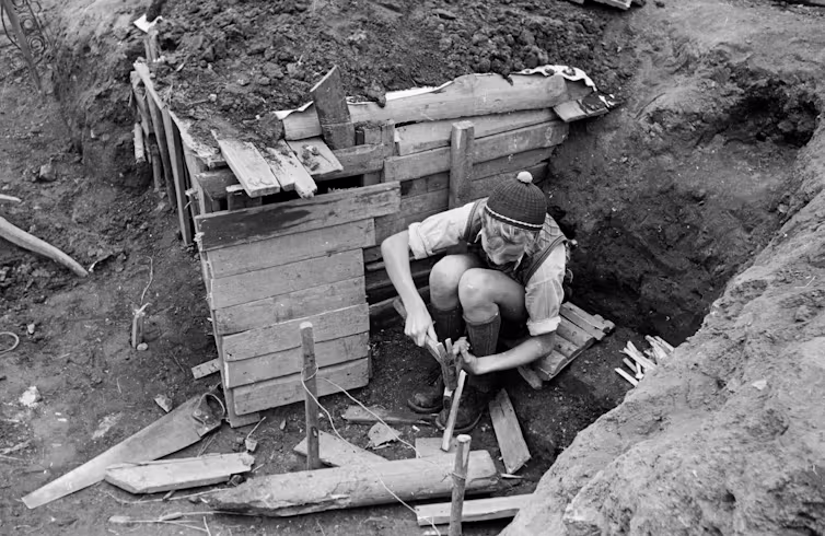 Photo en noir et blanc d’un garçon agenouillé dans un fossé et utilisant un marteau.