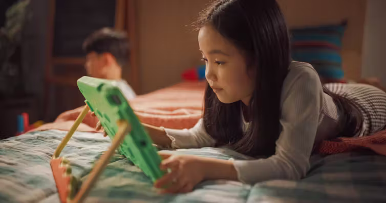 Fille allongée sur le lit, jouant sur une tablette