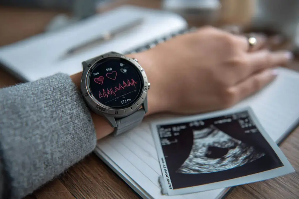 Gros plan sur une montre intelligente avec des données sur le sommeil à côté d’une échographie : technologie et maternité s’unissent pour mieux prendre en charge la grossesse à domicile.