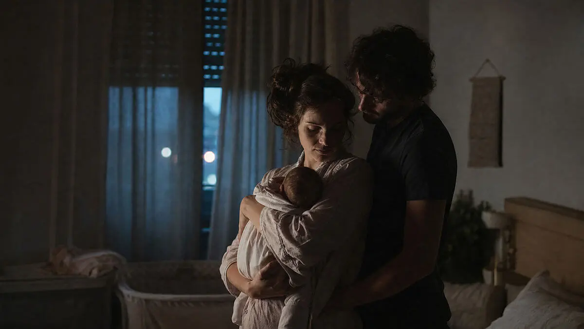 Nuit silencieuse avec horloge proche de 3 heures du matin, couple tenant bébé dans les bras, regard réfléchi, composition rétroéclairée