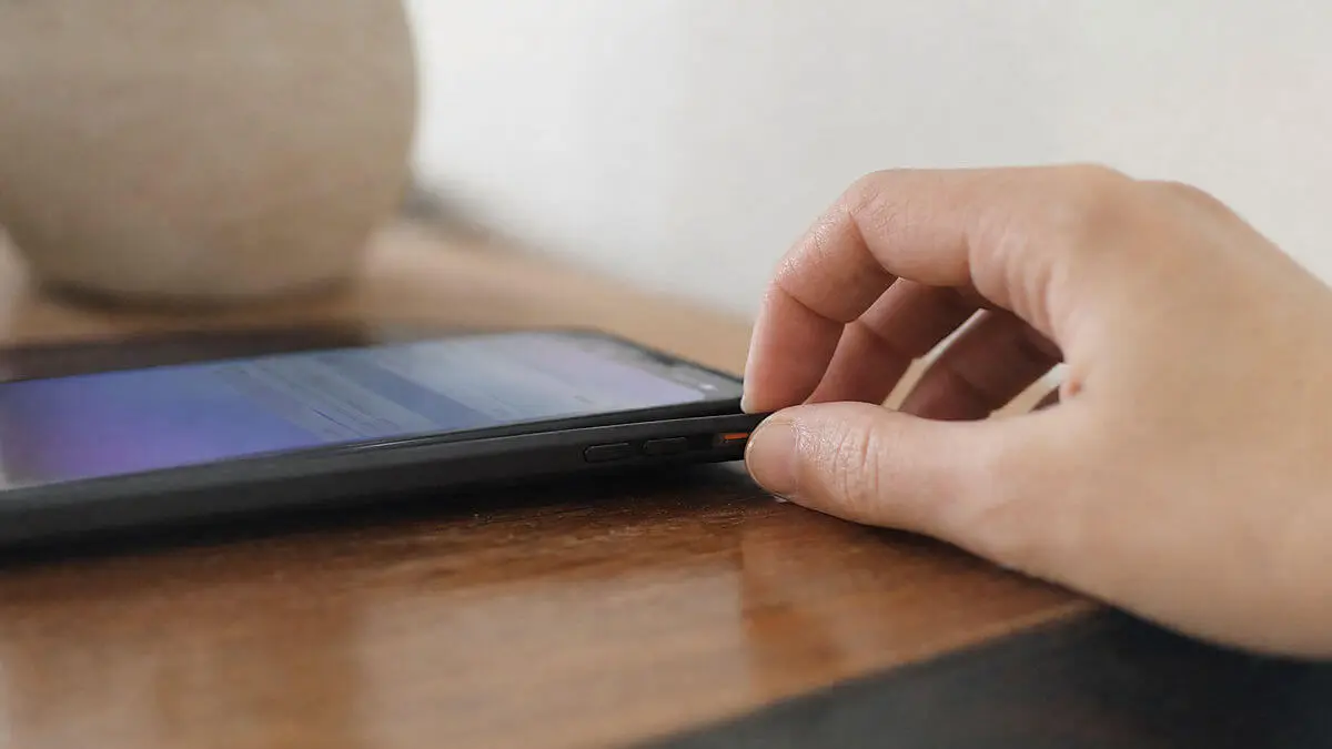 Gros plan d'un téléphone mobile avec écran et notifications flous, main plaçant le téléphone en mode silencieux ; environnement tra
