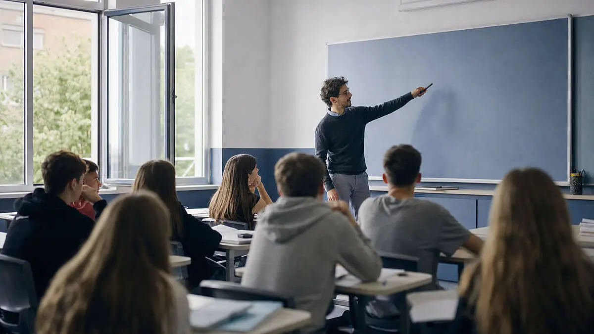 Salle de classe avec fenêtre ouverte sur l'extérieur : professeur guidant une activité stimulante au tableau, élèves attentifs